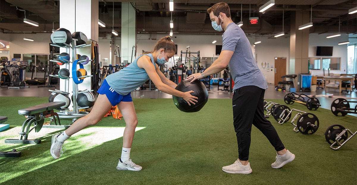 Bridge-Program_Lillian-Andrade-age-12-of-Dallas_Soccer_Knee_08-19-2021_070 Athlete and trainer using a medicine ball in a gym.