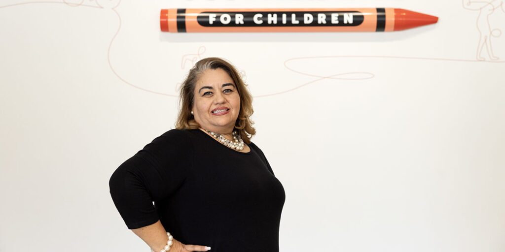 Elsa Guerrero poses in front of Scottish Rite for Children logo.