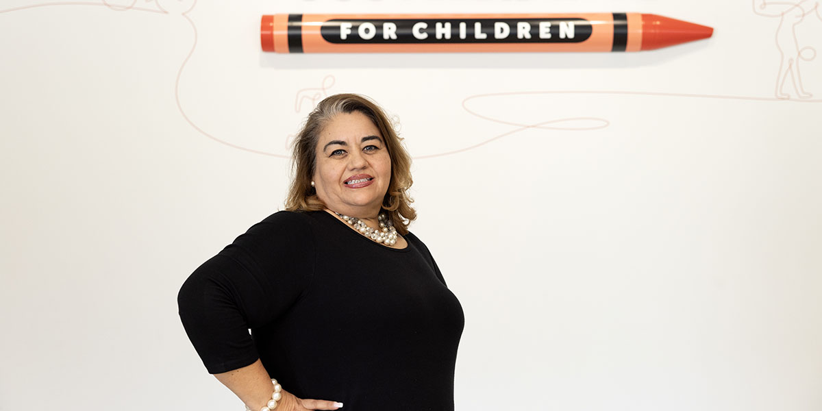 Elsa Guerrero poses in front of Scottish Rite for Children logo.