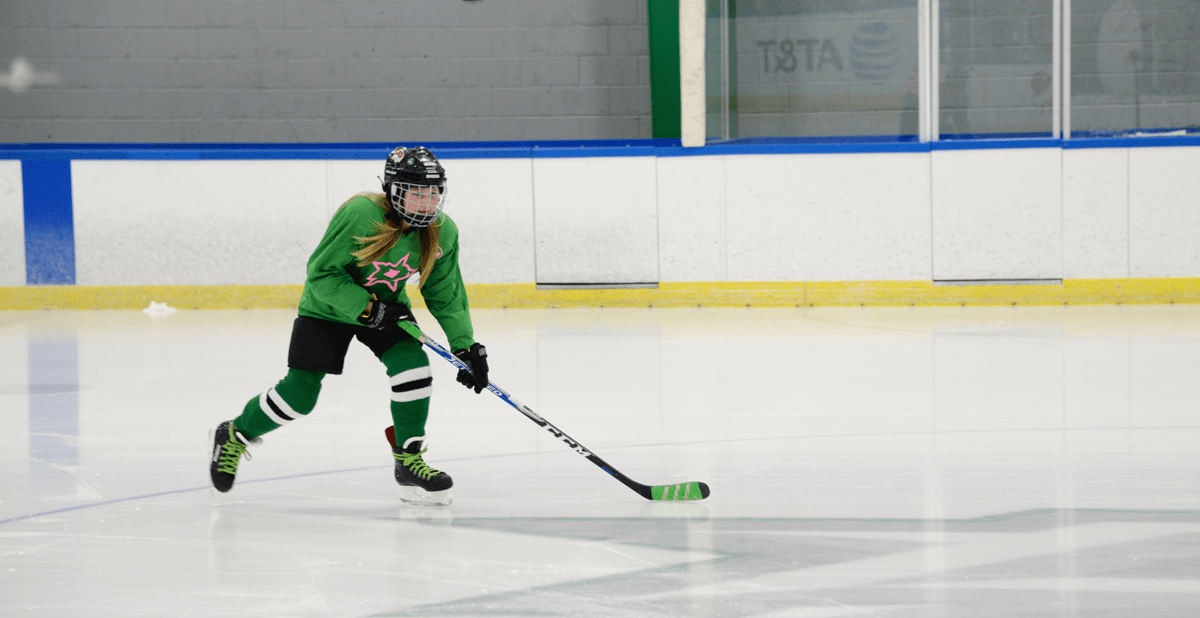 Young-Hockey-Player Female hockey player in green and black on ice rink.